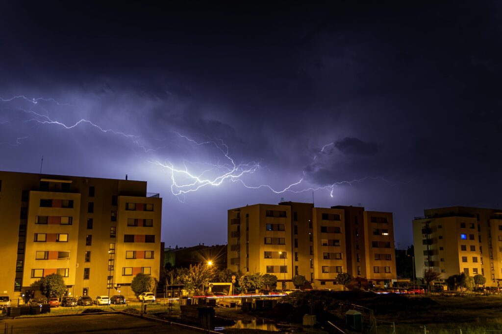 Lightning illuminates a dark sky over urban buildings at night.